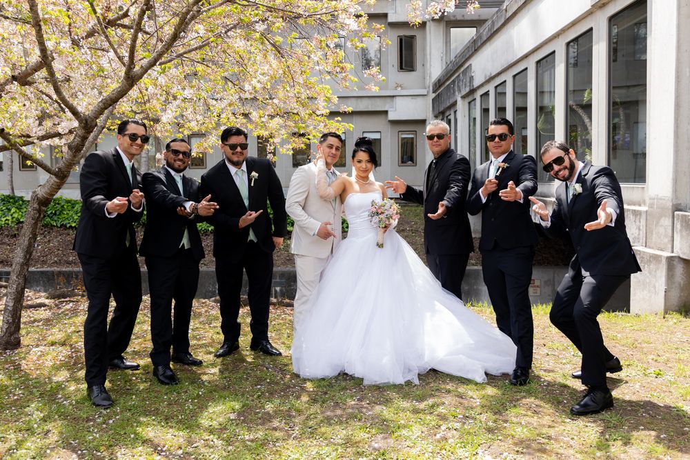 Wedding party in formal attire poses playfully on stone steps with autumn foliage in background.
