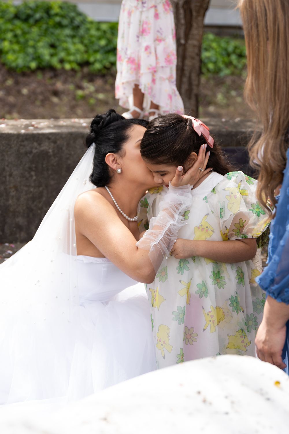 A couple shares a tender moment under white parasols at an outdoor wedding celebration.