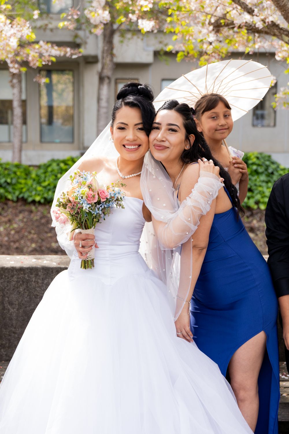 Wedding celebration outdoors with white bridal gown and navy blue bridesmaid dress visible among autumn foliage.
