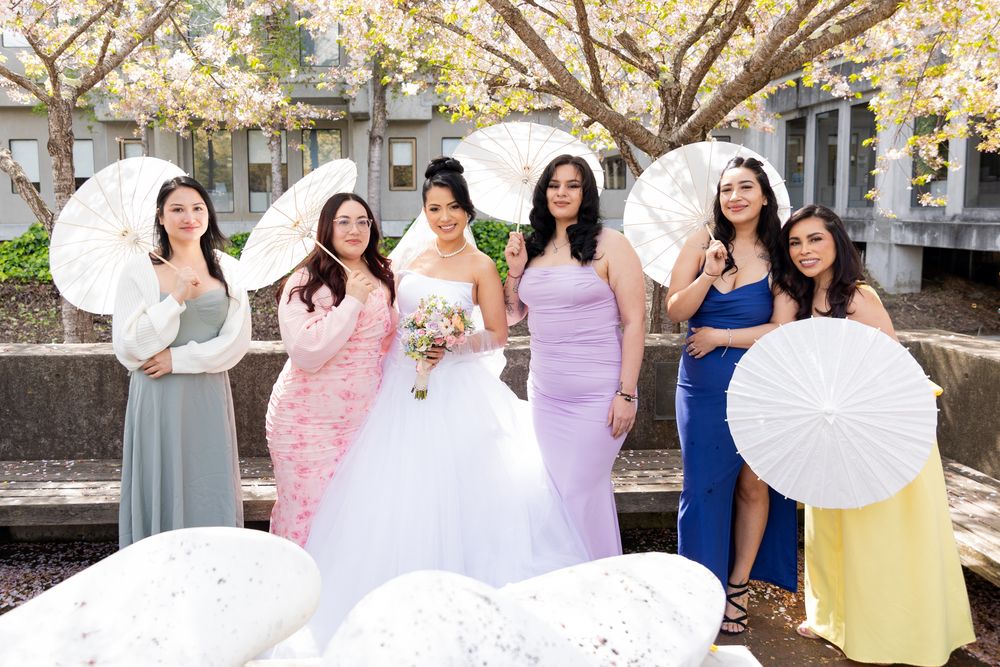 Wedding party poses with decorative white parasols in a garden setting.