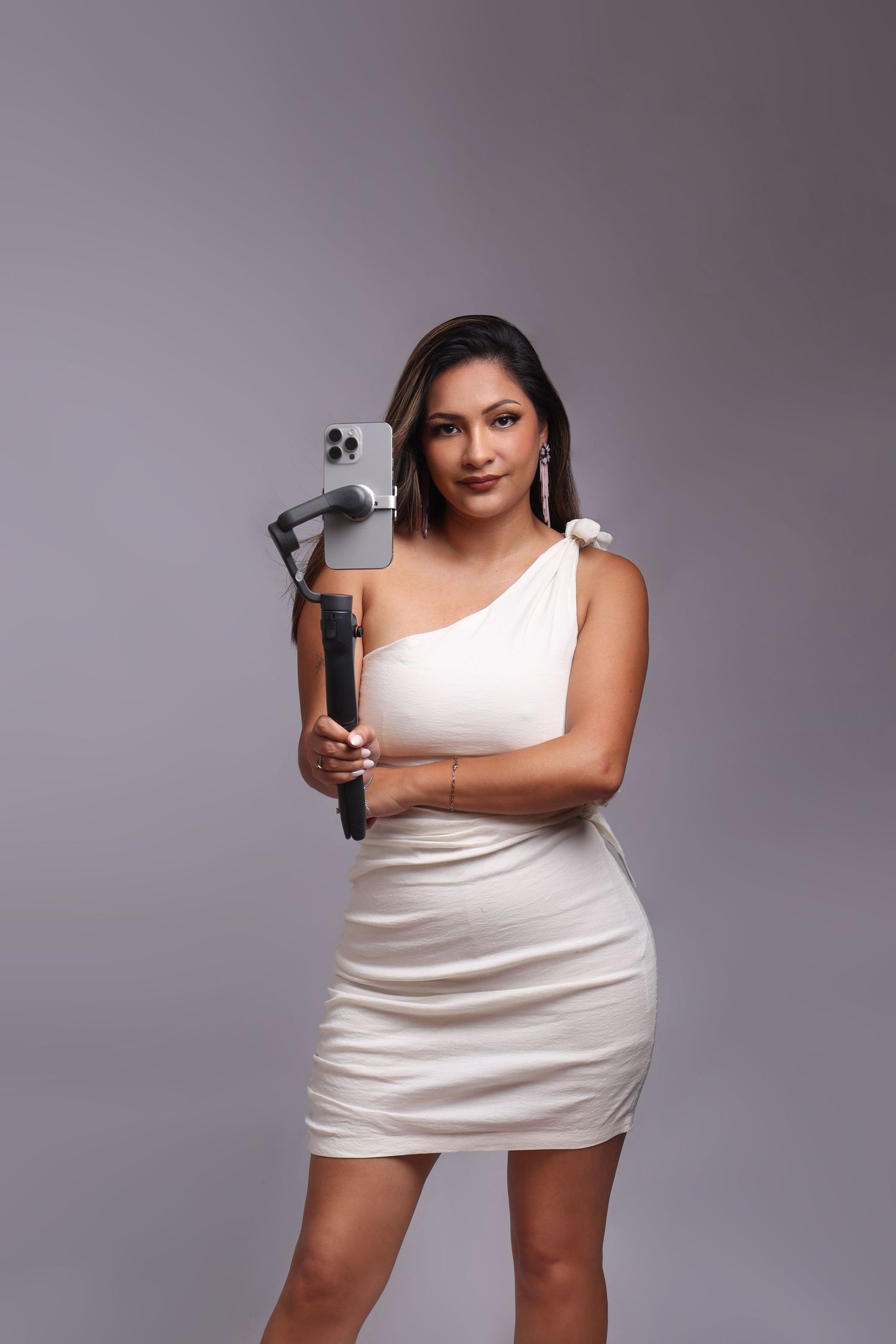 Professional photographer in black dress holding camera equipment against white backdrop.