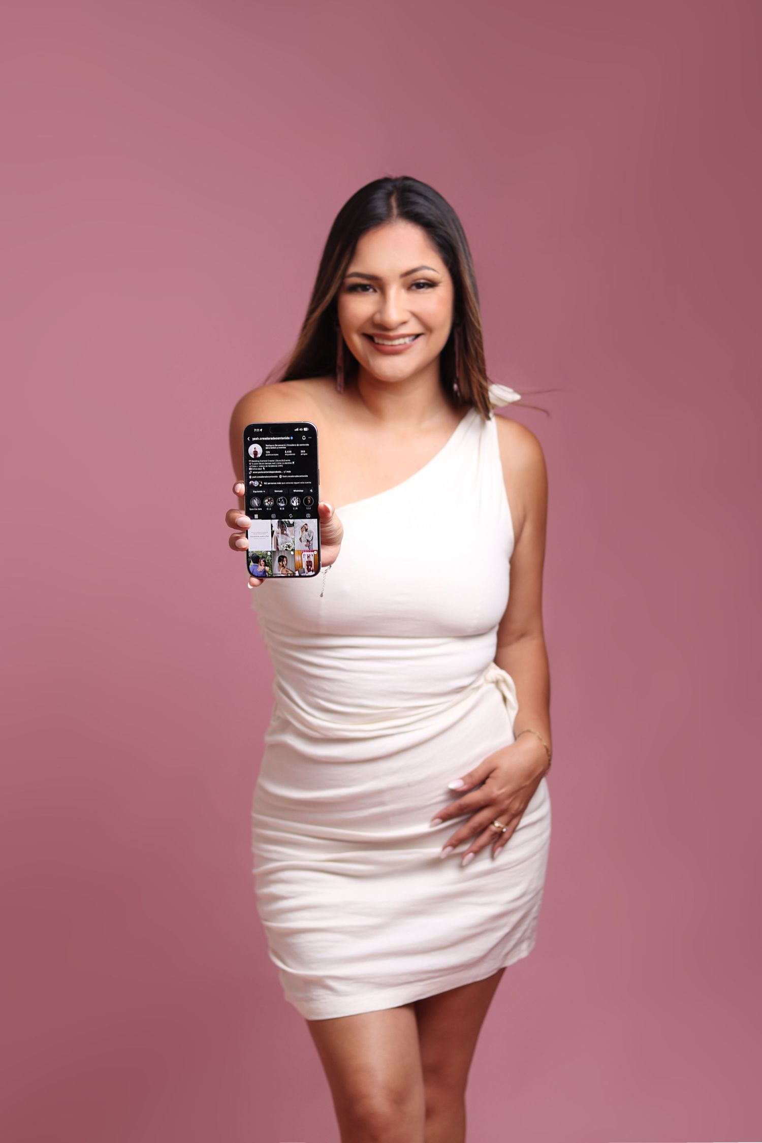 Professional photographer in black dress holding camera equipment against white backdrop.