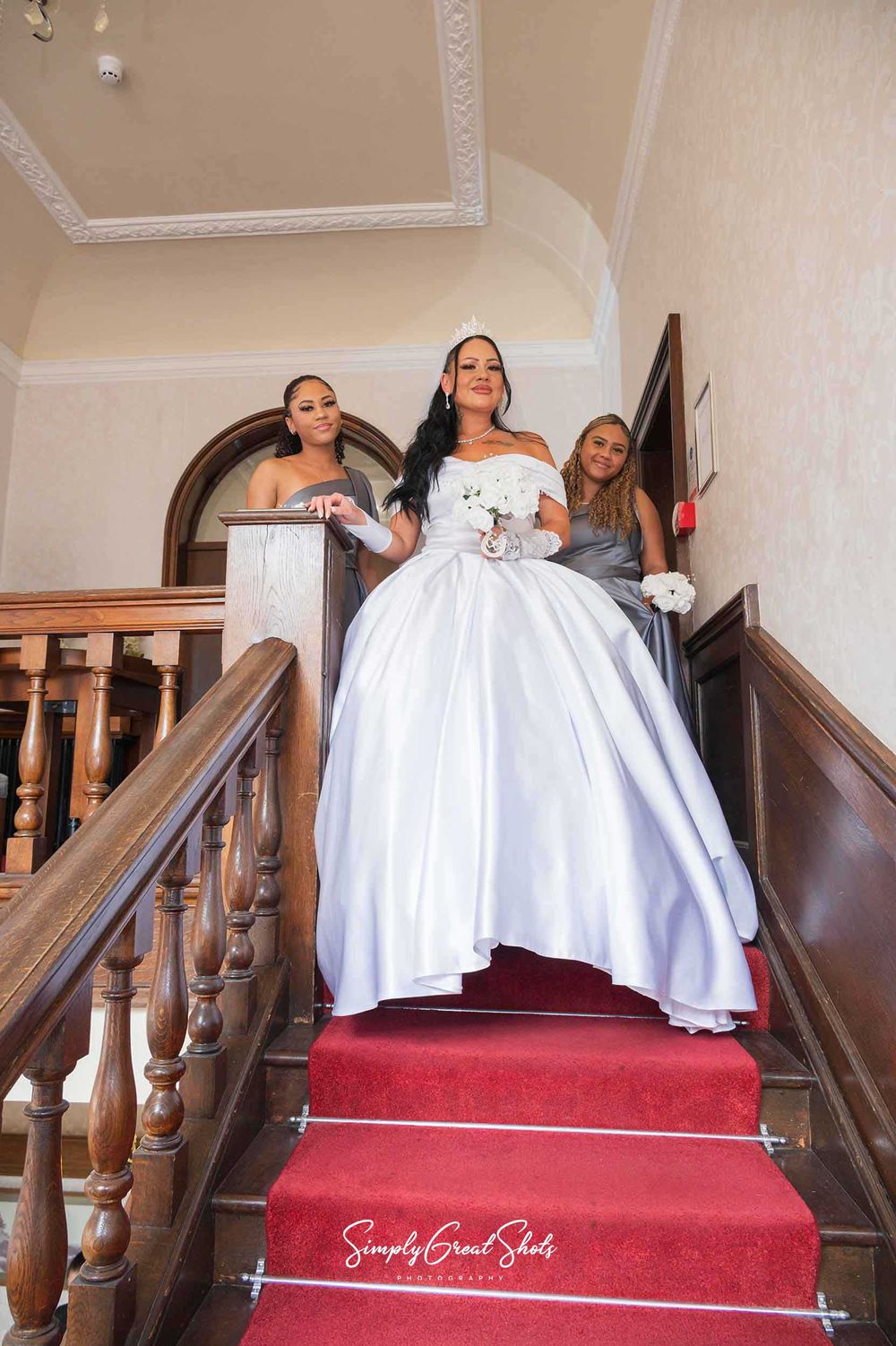 A bride and bridesmaids walk down the grand ornate staircase at Southcrest Manor Hotel in Redditch