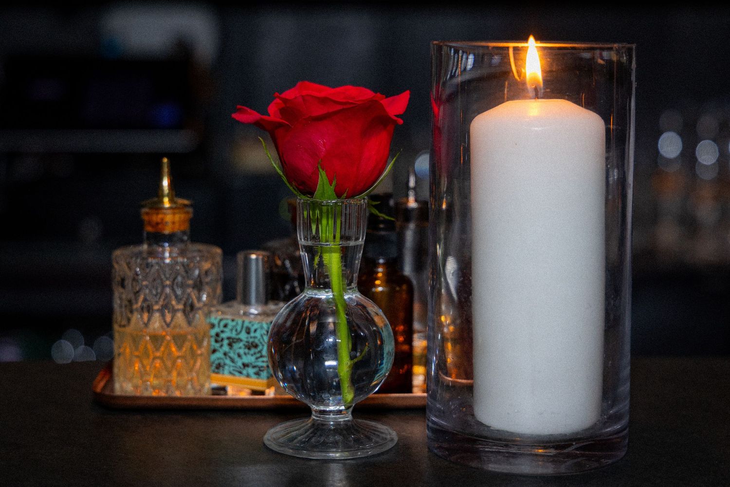 A romantic candlelit setting with a single red rose and glowing white pillar candles on a dark table.