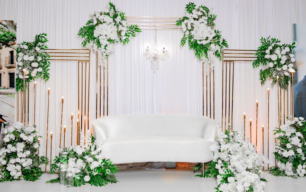 Elegant white wedding venue with copper arch details and cascading greenery garlands along the walls.