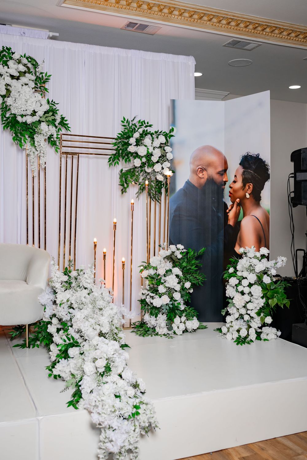 Elegant wedding ceremony setup with white floral arrangements, greenery accents, and modern architectural columns in a bright venue.