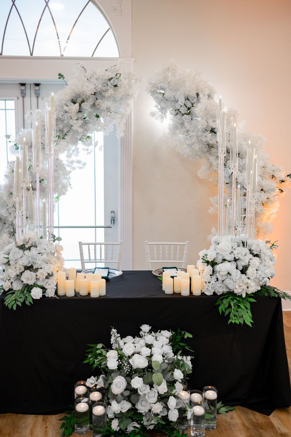 White floral arrangements with orchids and candles create an elegant wedding ceremony backdrop against a black draping.