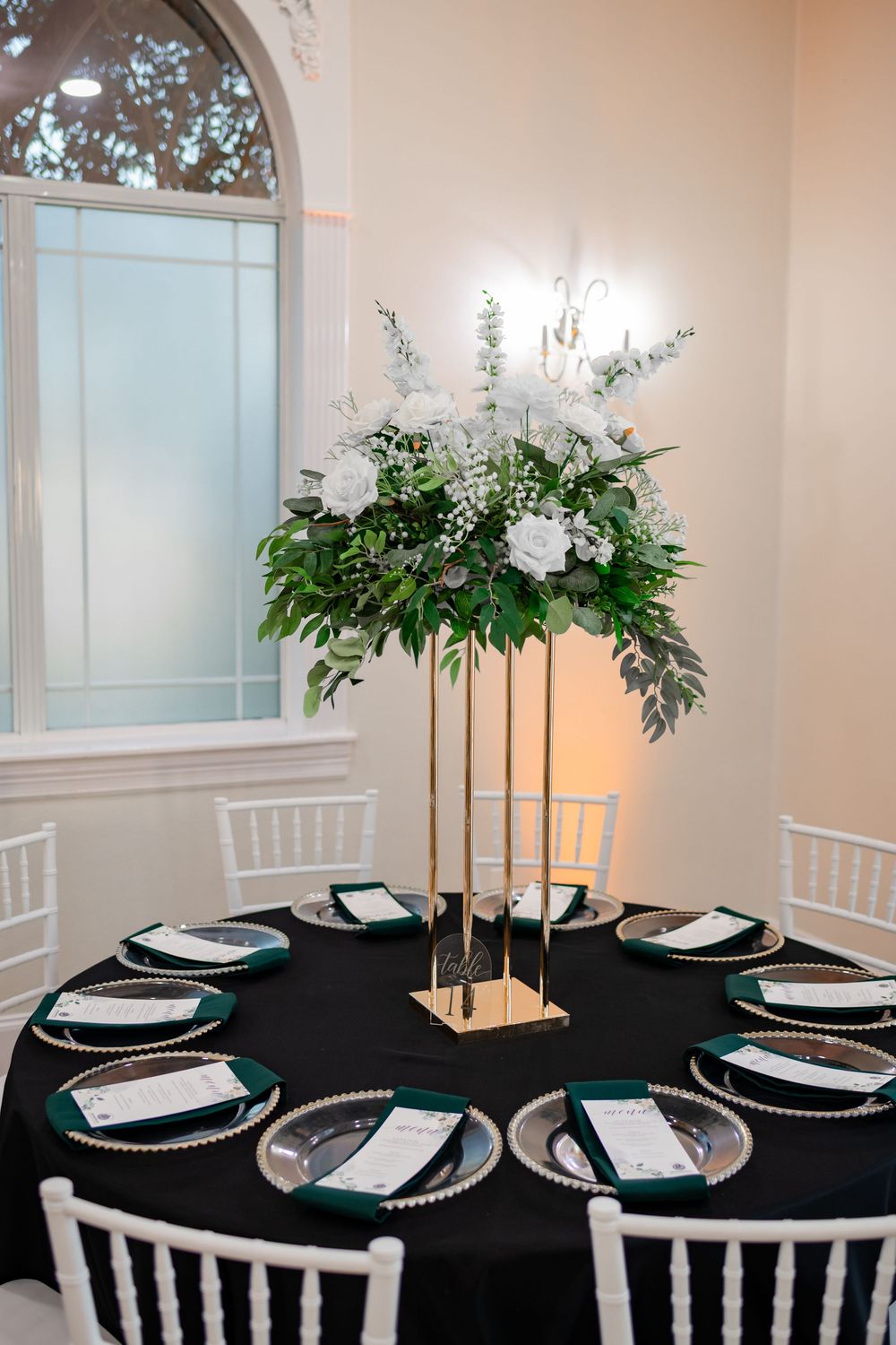 Elegant wedding reception table with black tablecloth, white place settings, tall candles and floral centerpieces.