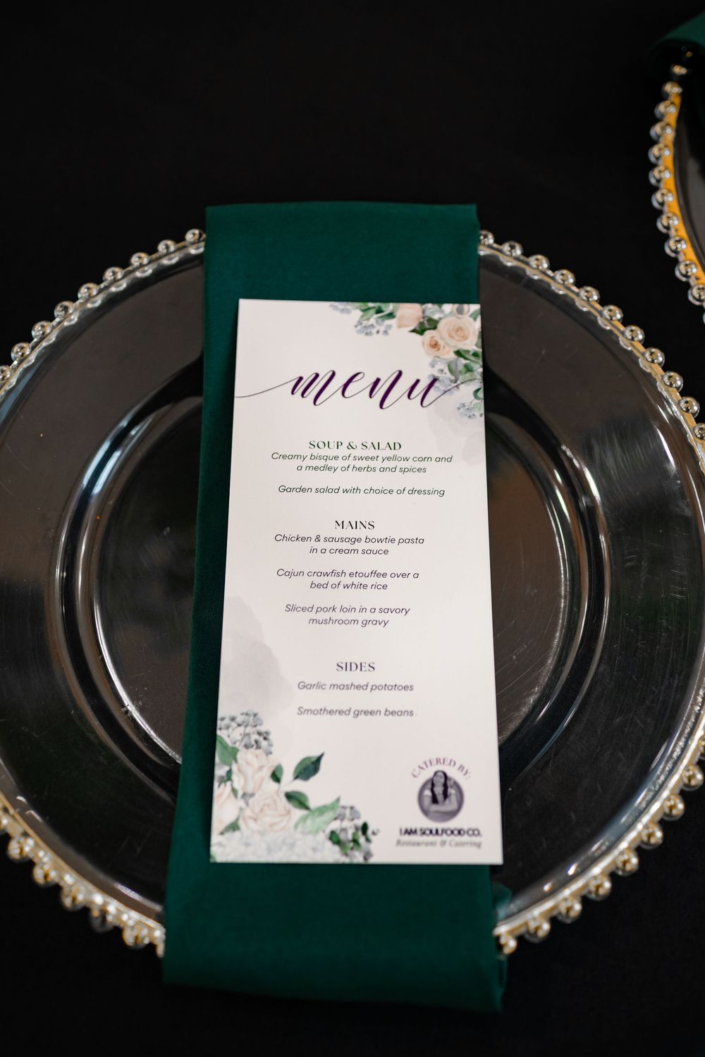Wedding menu cards with floral designs rest elegantly on black charger plates with pearl beaded edges.