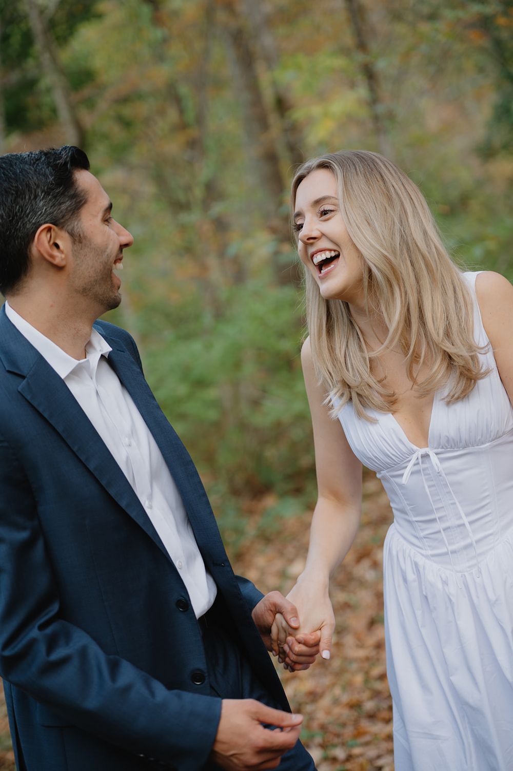 A couple laughs and embraces during an outdoor autumn photo session in a natural setting.
