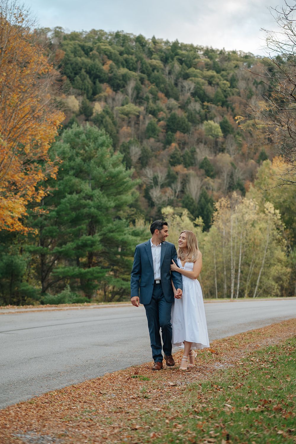 Couple walking and embracing on a scenic autumn road surrounded by colorful fall foliage and trees.