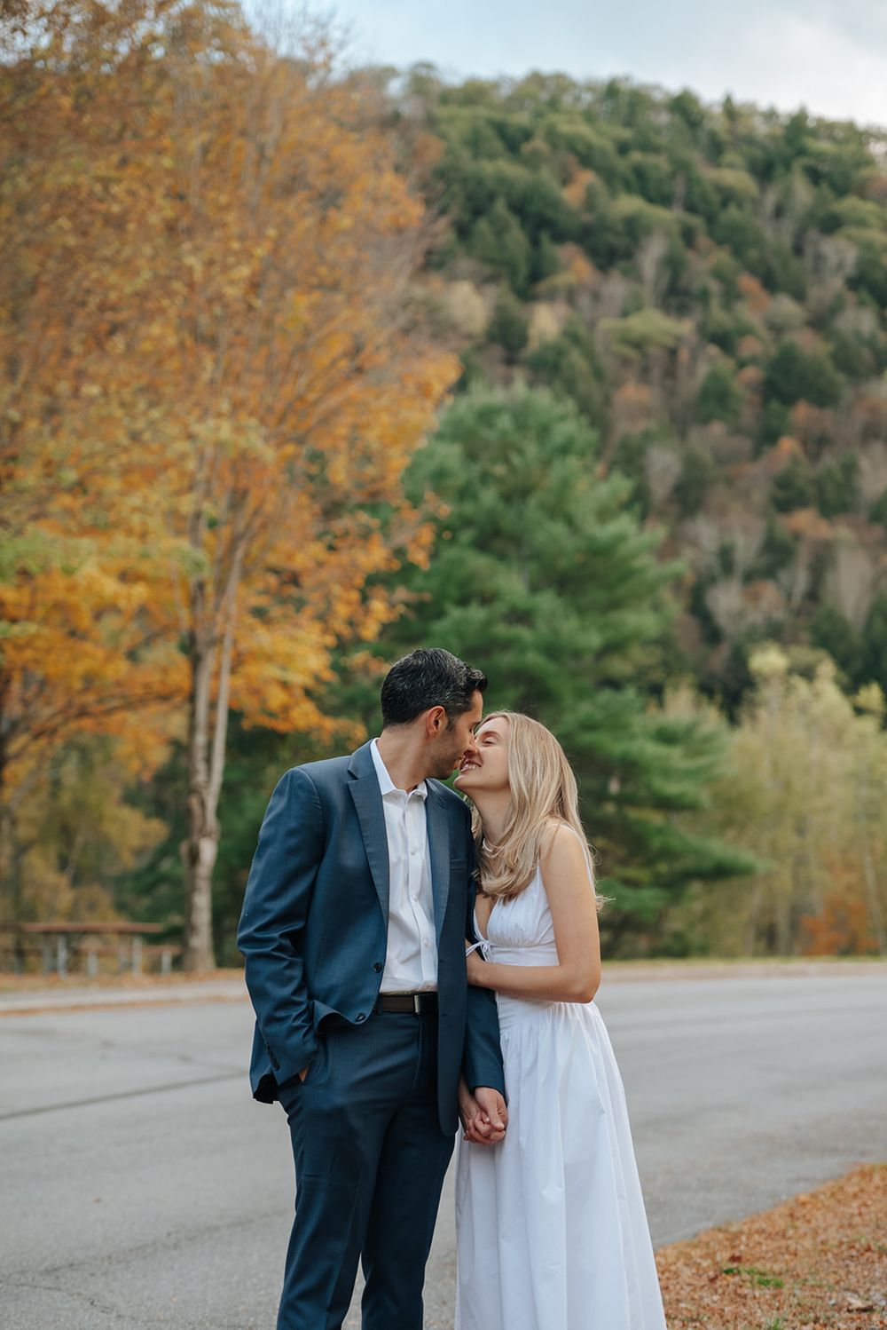 A romantic autumn wedding moment captured on a road lined with colorful fall foliage.