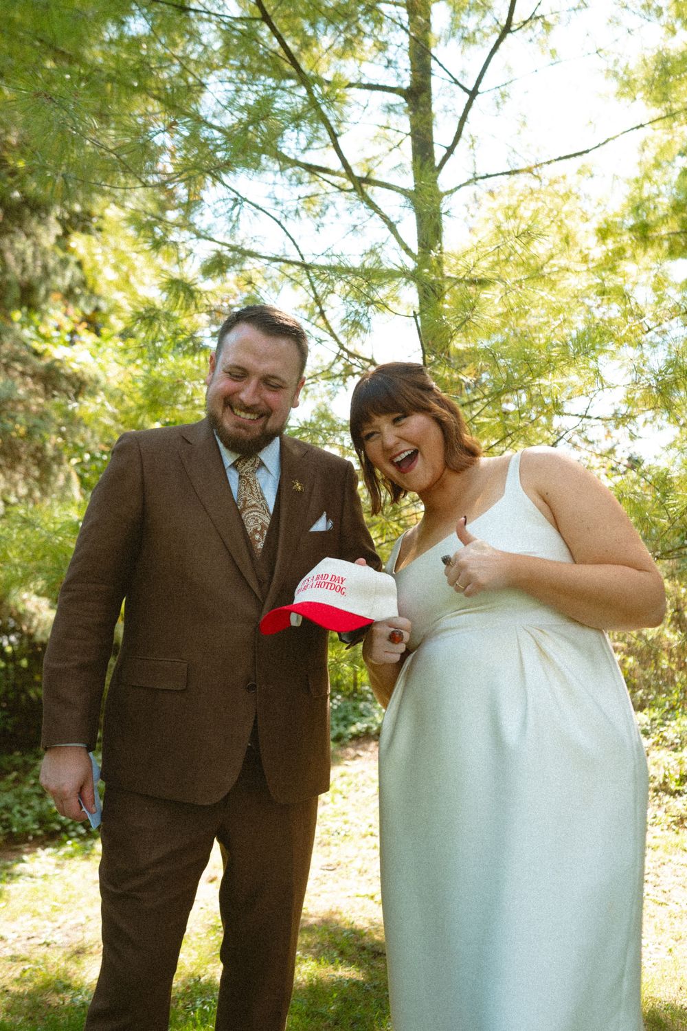 A happy couple shares a laugh together in a sunlit outdoor setting during their wedding day.
