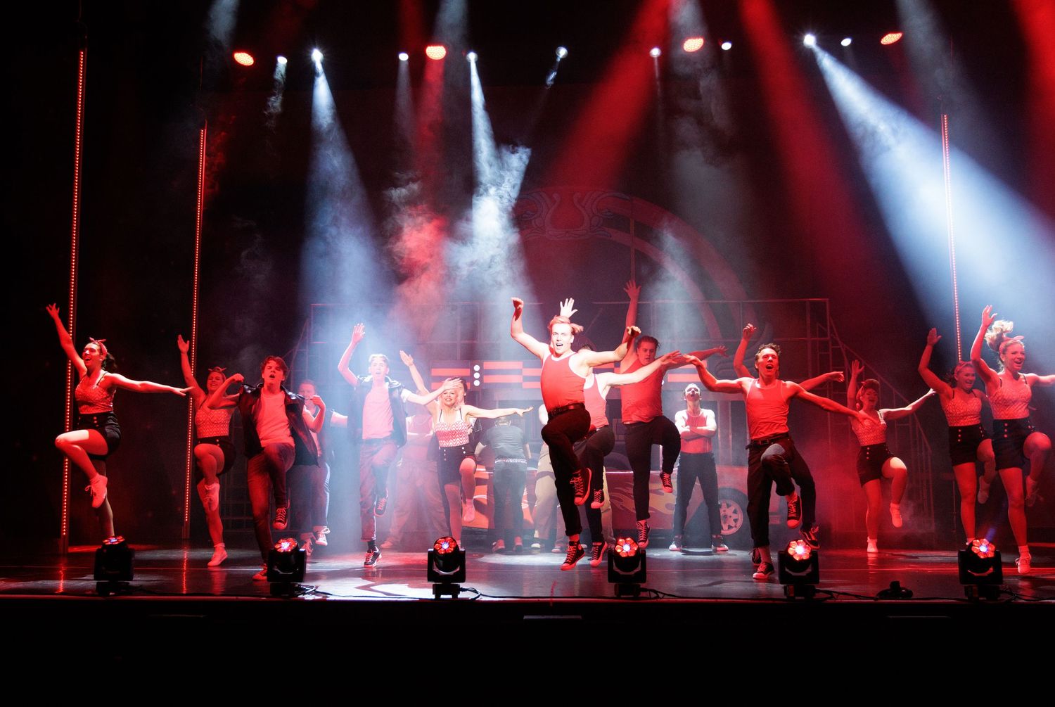 Silhouetted dancers perform on stage with dramatic red lighting and fog effects during a theatrical show.