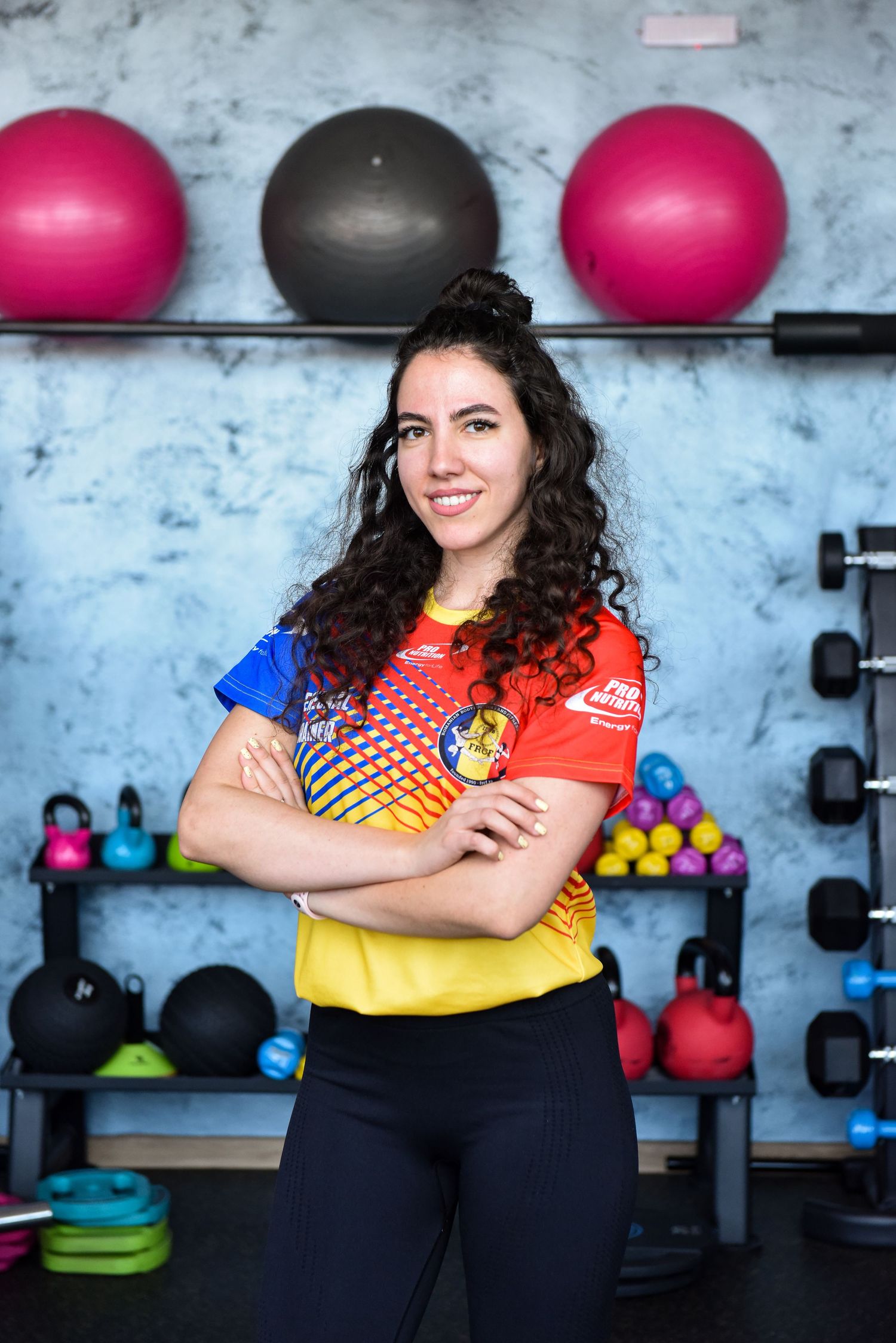 Fitness studio interior with colorful exercise balls and dumbbells visible on wall-mounted racks against blue wall.