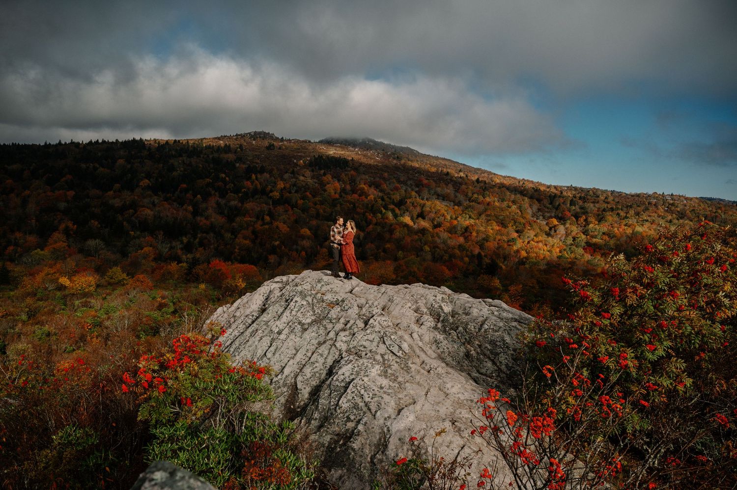 A scenic view of a rocky mountain trail surrounded by vibrant autumn foliage and dramatic cloudy skies.