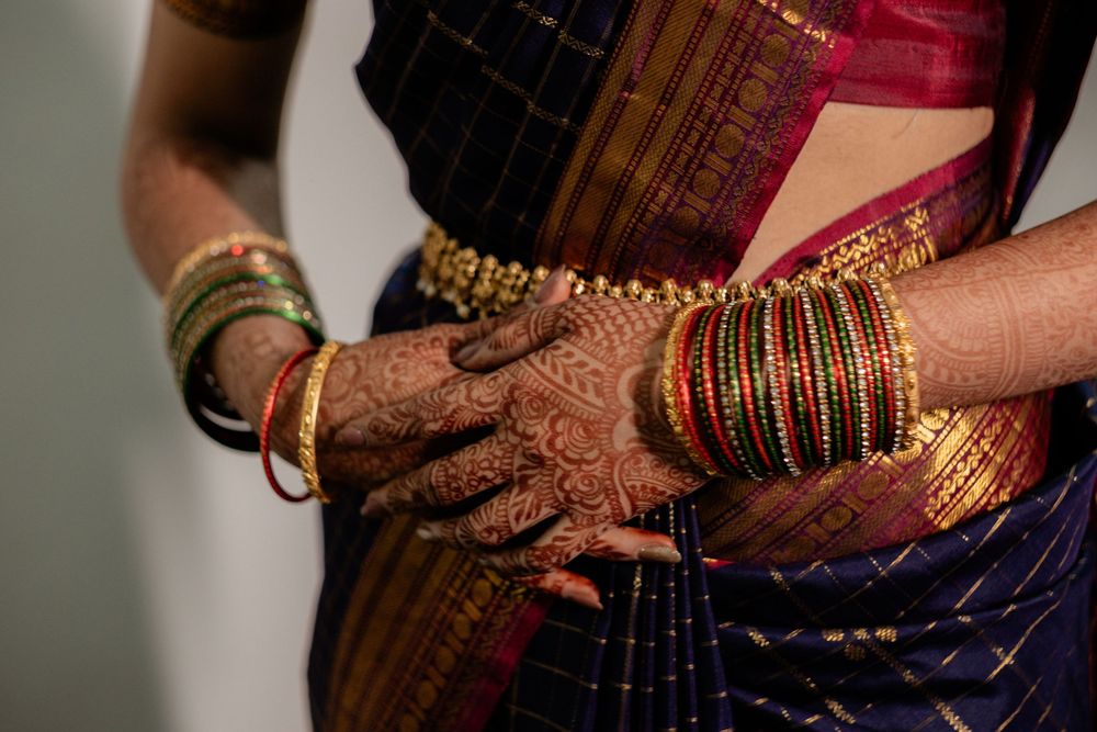 Traditional Indian gold bangles and jewelry displayed on hands and wrists against dark fabric.