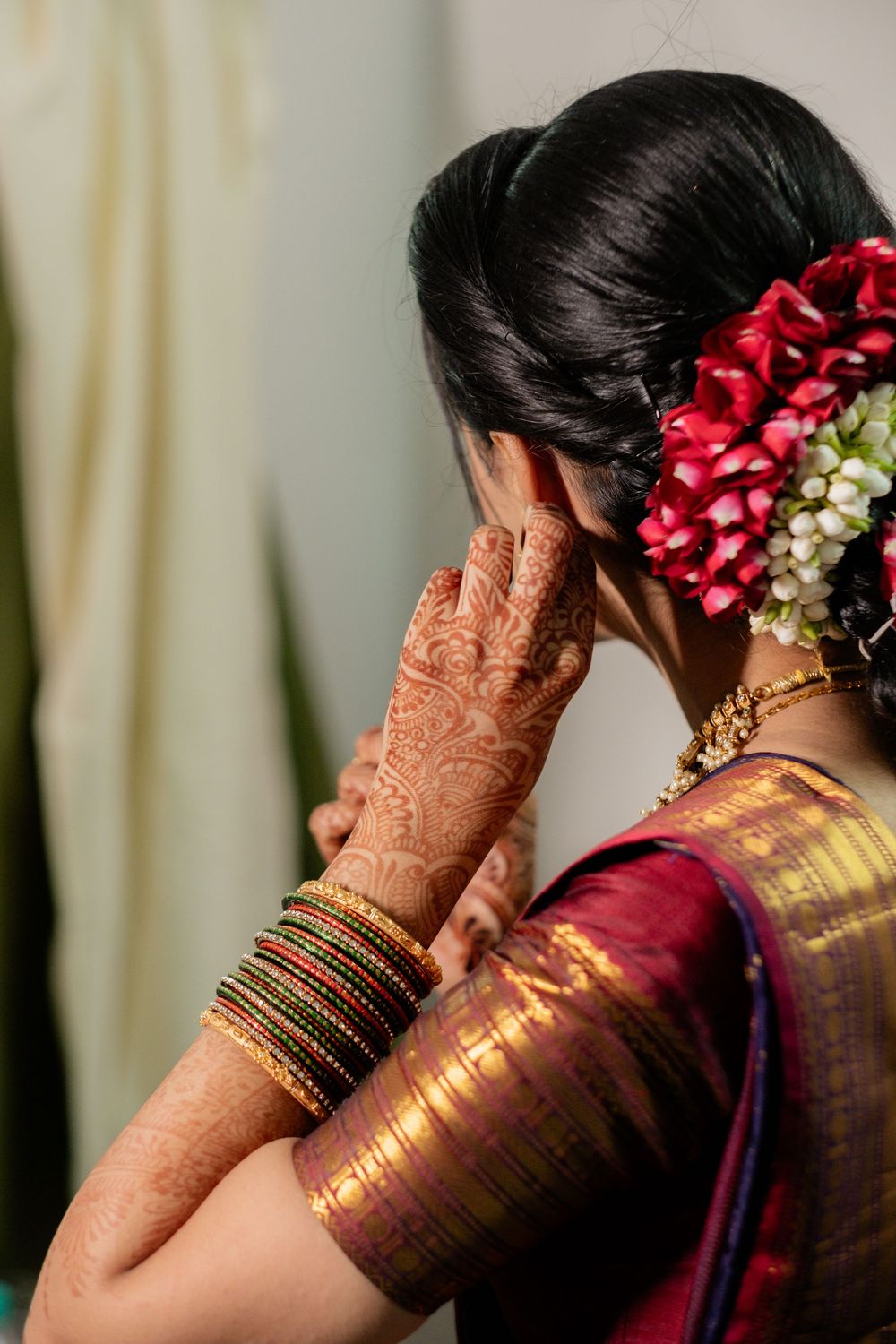 A close-up view of traditional Indian bridal details showing intricate henna designs, bangles and red floral hair accessories.