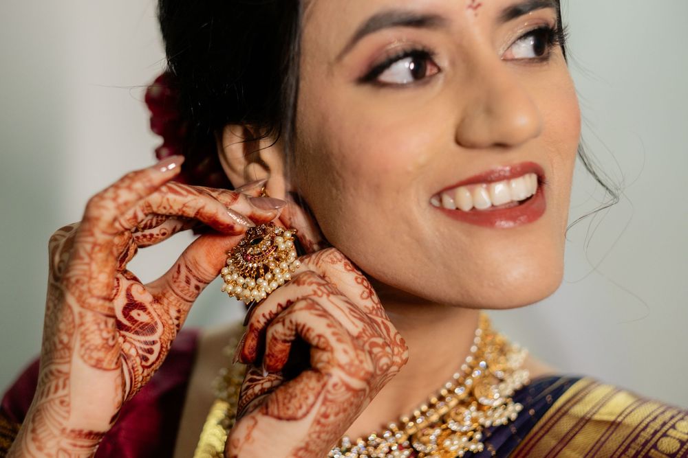 Bride wearing traditional Indian wedding jewelry and makeup smiling during preparation.