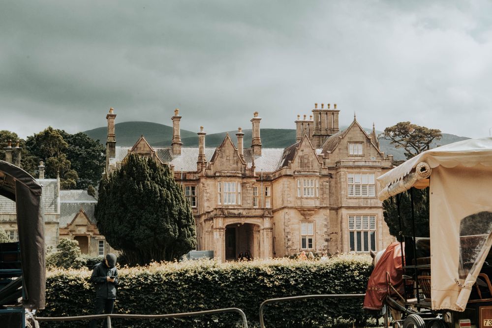 Row of elegant Victorian mansions with ornate architectural details line a residential street under cloudy skies.