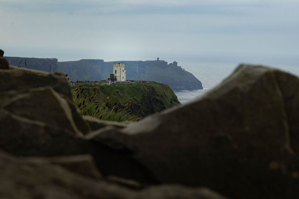 Distant lighthouse perched on rugged coastal cliffs overlooking a misty ocean horizon.