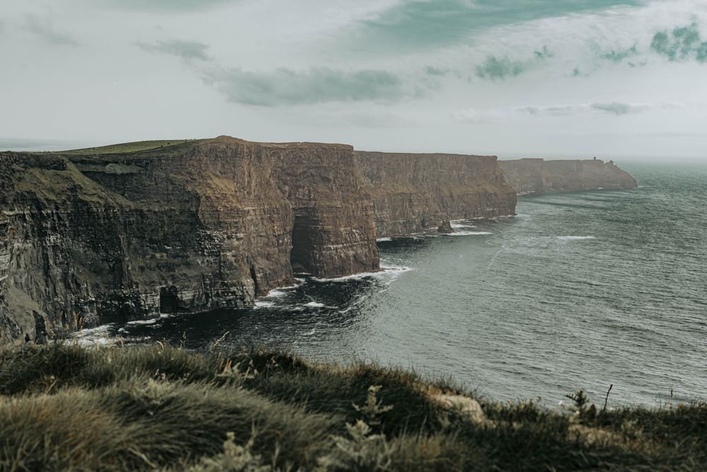 Dramatic coastal cliffs rise above the misty ocean along a rugged shoreline under moody gray skies.
