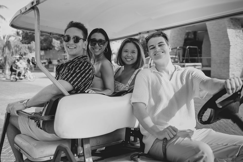 Young people smile while riding together in a golf cart in this black and white photograph.