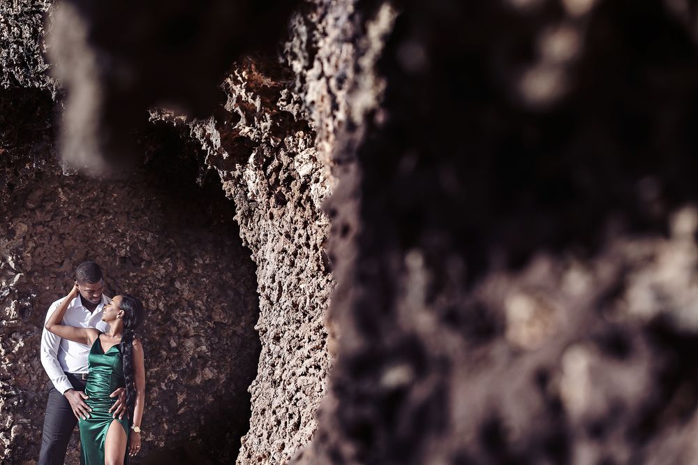 A couple embraces against a textured rock wall in an artistic outdoor photoshoot.