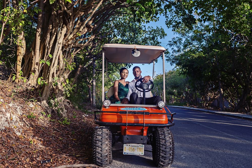 Golf cart driving down a paved road with green foliage on a sunny day.