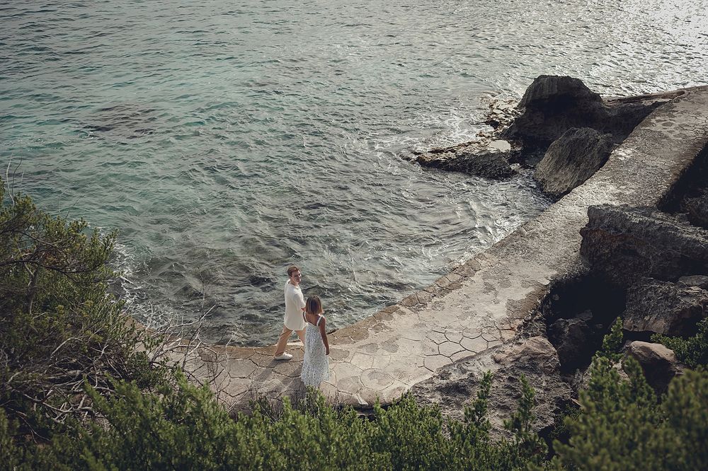 Rocky cliff coastline with waves crashing against stone formations and turquoise waters beneath a cloudy sky.