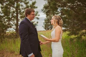 Two people exchange vows during an outdoor wedding ceremony with a forest backdrop.