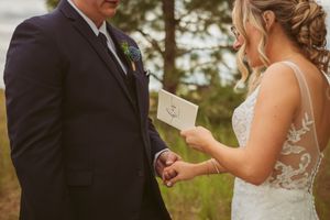 A wedding couple exchanging vows during an outdoor ceremony surrounded by trees and greenery.