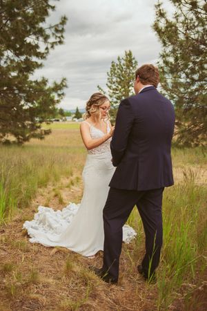 Wedding couple sharing an intimate first look moment in a rustic outdoor field surrounded by pine trees.