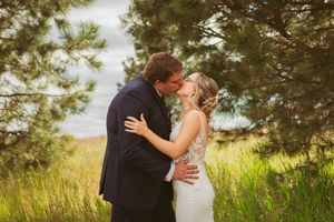 A romantic wedding moment captured outdoors with evergreen trees and tall grass in the background.