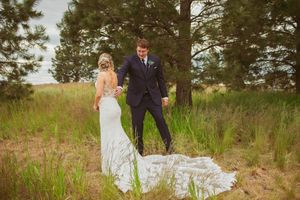 A beautiful wedding couple embraces in a grassy meadow surrounded by towering pine trees.