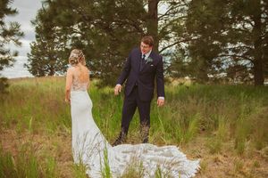 A bride in a flowing white dress walks through a scenic outdoor setting with pine trees.