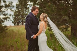 Wedding couple stands together in a romantic moment against evergreen trees and rolling hills.