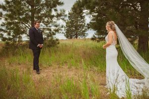 A formal couple embracing in a romantic outdoor setting with tall grass and pine trees in the background.