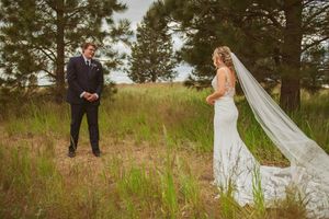 Bride in flowing veil and groom share emotional first look moment in natural outdoor setting.
