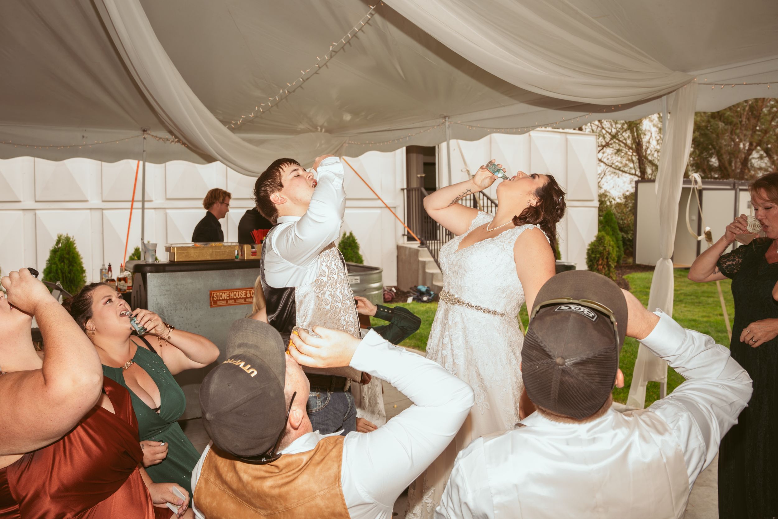 Wedding reception guests in a white tent joyfully dance and drink champagne during the celebration.