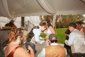 Couples slow dance beneath elegant white tent draping with string lights at sunset during a wedding reception.