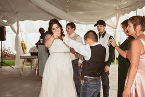 Wedding guests dance together under a white tent during an outdoor reception celebration.