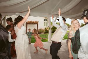 Wedding guests dancing and celebrating under a white tent canopy at an outdoor reception.