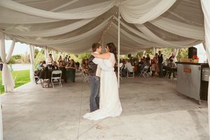 Two people share a romantic first dance under an elegant draped tent canopy at an outdoor wedding reception.