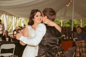 Dancing couple embrace during the first dance at their wedding reception under a tent with string lights.