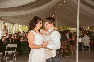 Wedding couples share intimate dances under a large white tent decorated with twinkle lights and fabric draping.