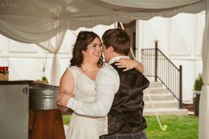 A couple enjoys their first dance together under a white tent canopy at an outdoor wedding reception.
