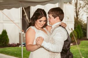 Bride and groom share an intimate dance together under a white tent at an outdoor wedding reception.