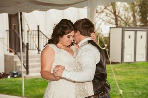 A romantic couple shares their first dance under a white tent on a green lawn during their wedding celebration.