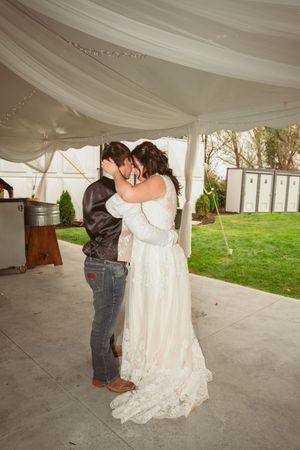 A couple shares their first kiss as newlyweds under an elegant white tent during their outdoor wedding reception.